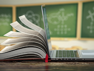 book open against back of laptop with chalkboards in background